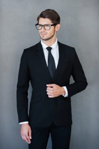 Confident young businessman adjusting his jacket and looking away while standing against grey background